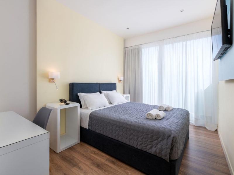 Eenvoudige hotelkamer met groot bed, nachtkastjes en aan de muur gemonteerde tv.