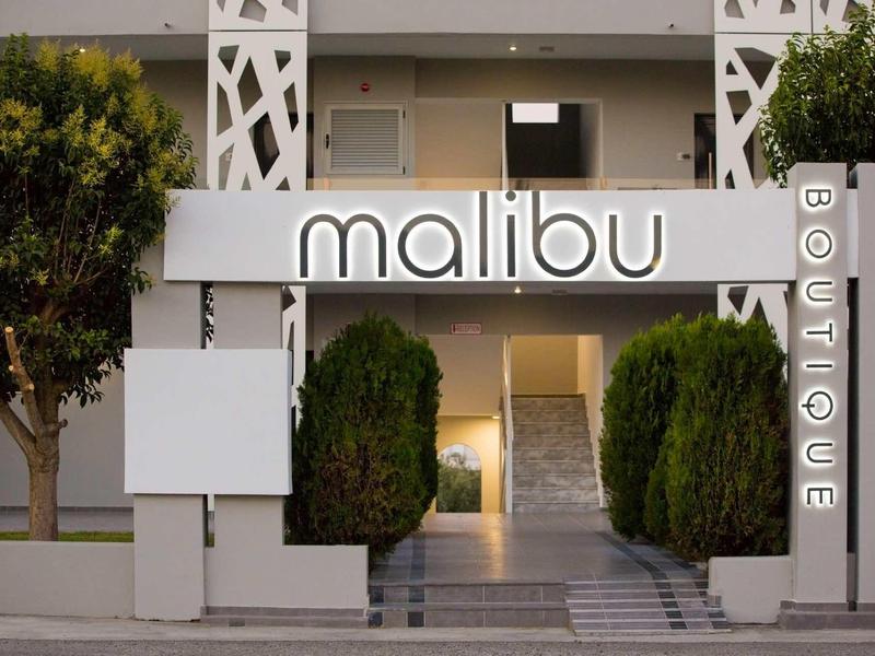 Entrance with 'malibu BOUTIQUE' sign and pathway, flanked by two bushes and building facade.