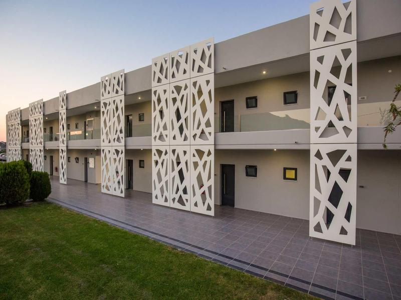 Modern hotel building with decorative white panels and well-kept lawn at sunset.