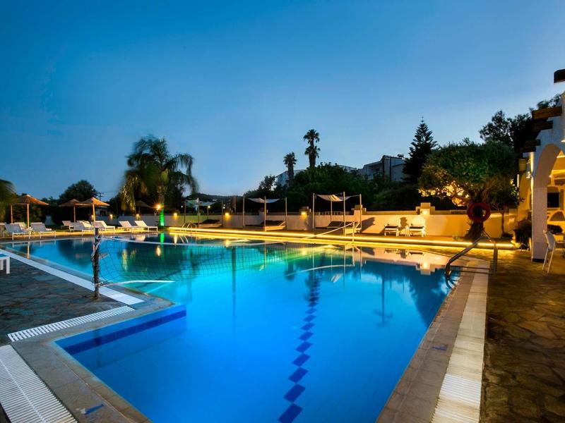 Illuminated hotel pool at sunset with lounge chairs and palm trees in the background.
