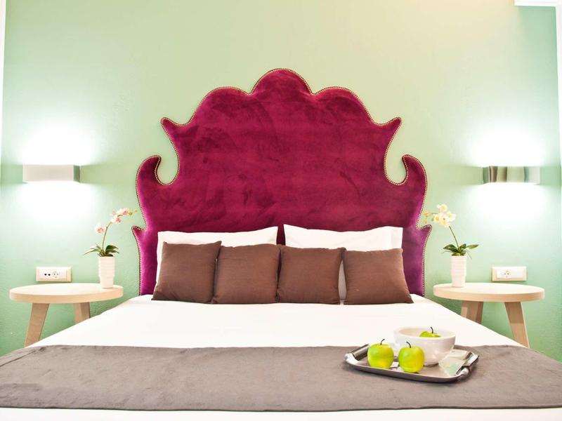 Cozy bed with decorative purple headboard and bedside tables in a light green room.
