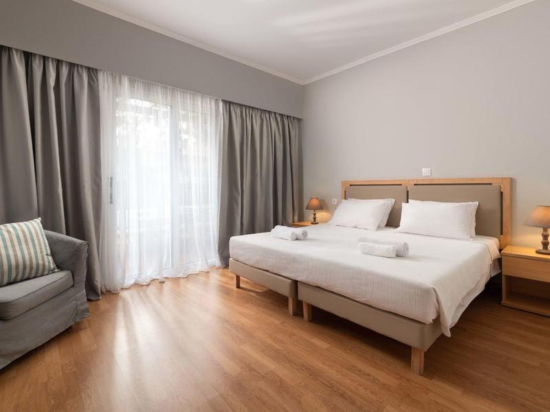 Cozy hotel room with double bed, armchair, and wooden floor in daylight.