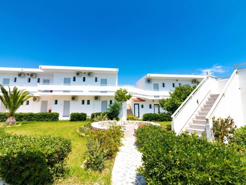 White hotel buildings with balconies and greenery under a clear blue sky.