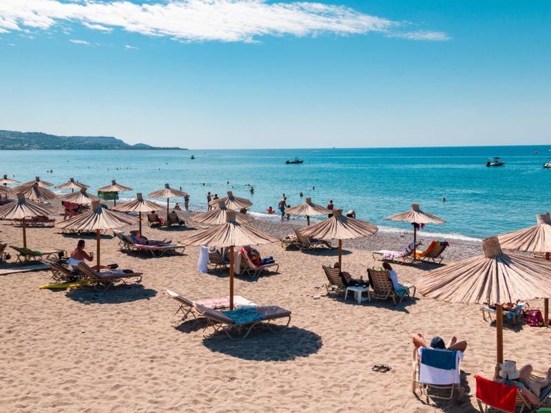 Sandy beach with many sun umbrellas and guests under a blue sky by the sea.