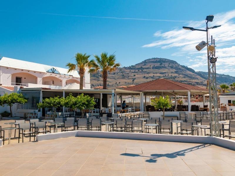 Open seating area with tables and chairs in front of a hotel with palm trees and mountains in the background.