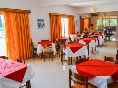 Comedor luminoso con mesas cubiertas con manteles rojos y blancos y cortinas naranjas.