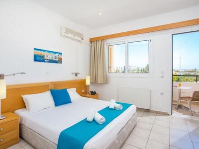 Camera d'hotel luminosa con letto matrimoniale, accenti blu e balcone con vista sulla città.