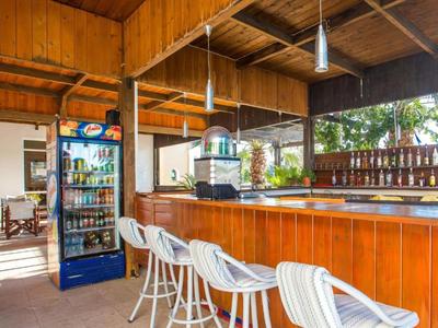 Área de bar abierta en hotel con mostrador de madera, sillas altas blancas y refrigerador de bebidas.