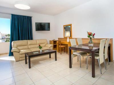 Soggiorno luminoso con divano beige, tavolo da pranzo, sedie, TV e balcone con vista laterale.