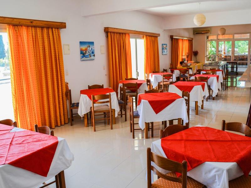 Sala da pranzo luminosa con tende arancioni e tavoli con tovaglie rosse.