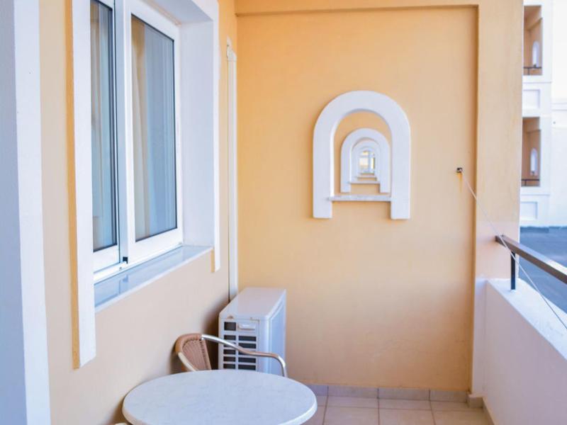 Balcone con pareti beige, tavolo rotondo bianco e due sedie accanto a finestra e ringhiera.