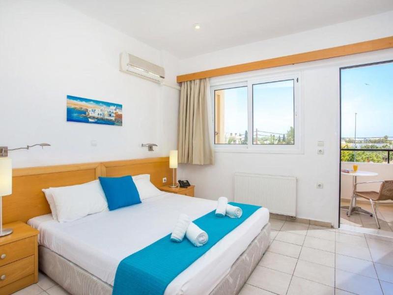 Camera d'hotel luminosa con letto matrimoniale, accenti blu e balcone con vista sulla città.