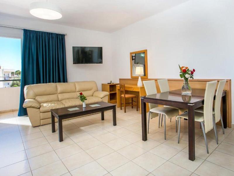 Soggiorno luminoso con divano beige, tavolo da pranzo, sedie, TV e balcone con vista laterale.