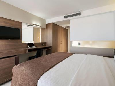 Modern hotel room with large bed, brown blanket, and wall-mounted TV.