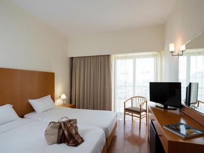 Bright hotel room with two single beds, TV on a desk, and a chair by the window.