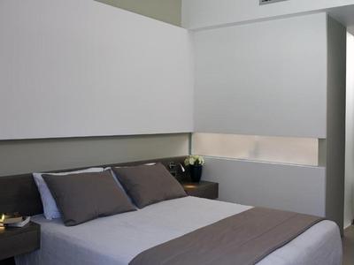Modern hotel room with double bed, gray pillows, and minimalist design.