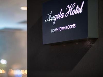 Black hotel sign with white text 'Angela Hotel Downtown Rooms' on a dark wall.