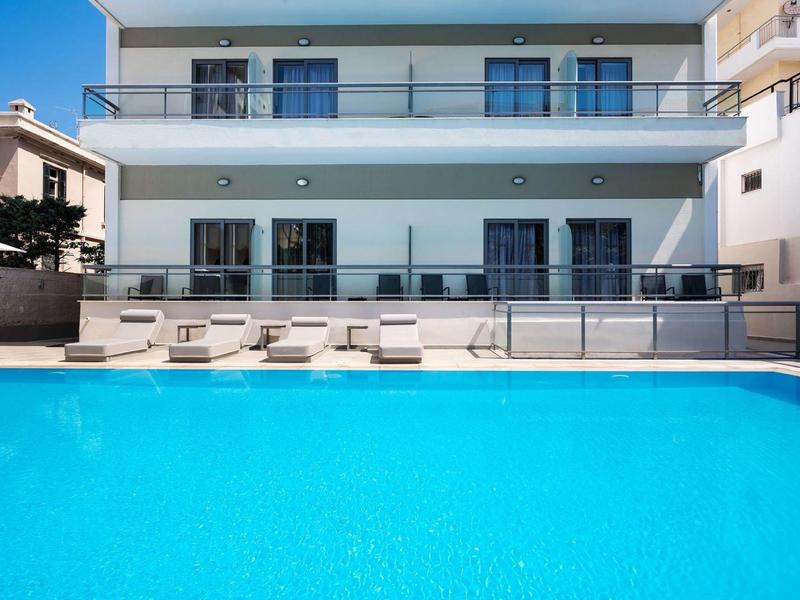 Modern hotel pool with lounge chairs in front of a white building with balconies.