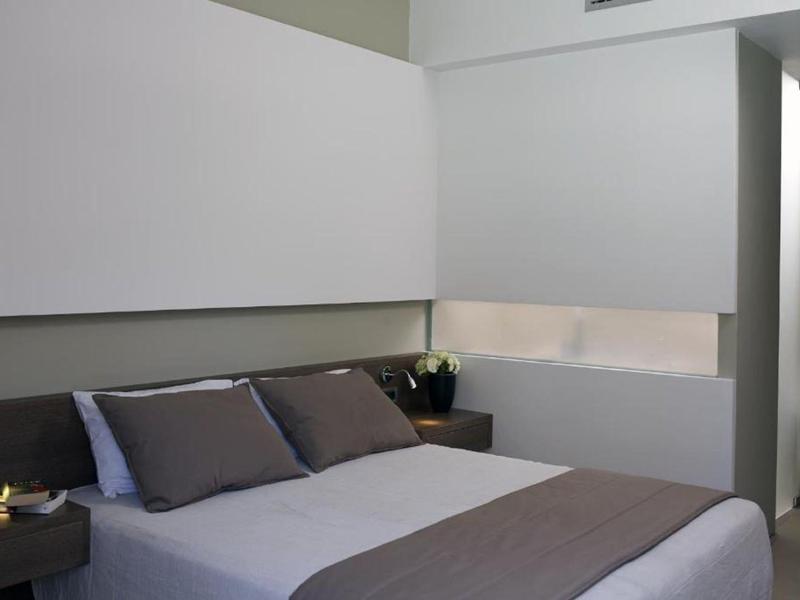 Modern hotel room with double bed, gray pillows, and minimalist design.