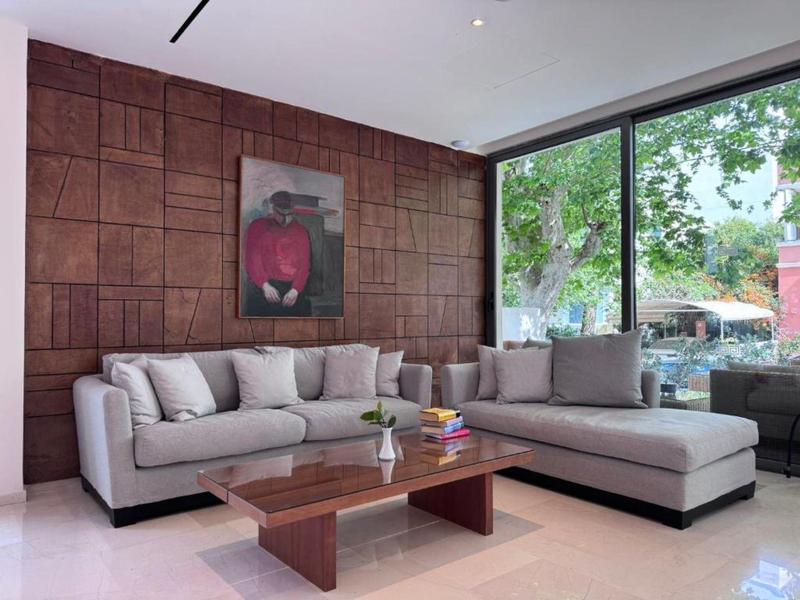 Modern living room with gray sectional sofa, wood-paneled wall, and large windows overlooking a garden.