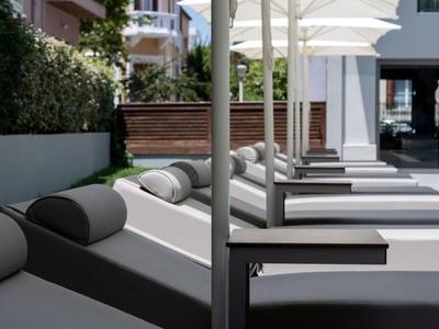 Lettini moderni all'aperto con cuscini grigi e ombrelloni bianchi vicino a una piscina d'hotel.