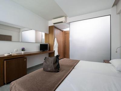 Modern hotel room with double bed, desk, mirrors, and simple decor.