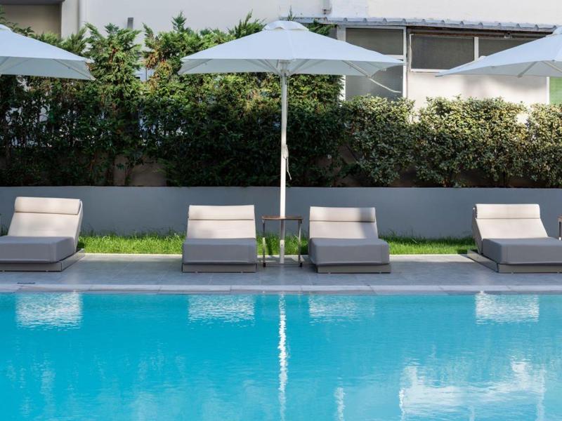 Four sun loungers under white umbrellas next to a blue swimming pool.