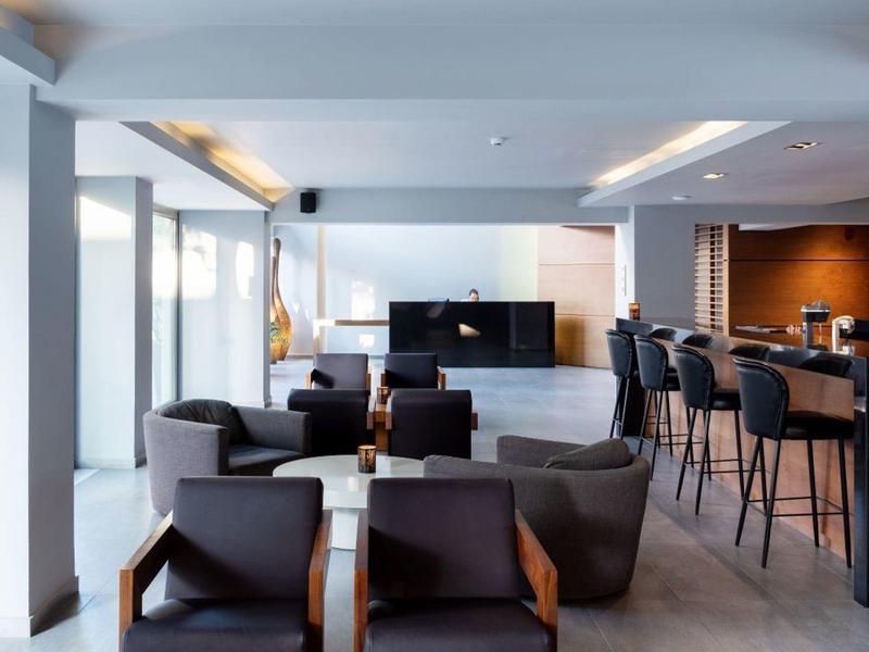 Modern hotel lounge with armchairs, bar stools, and a large wall-mounted TV.
