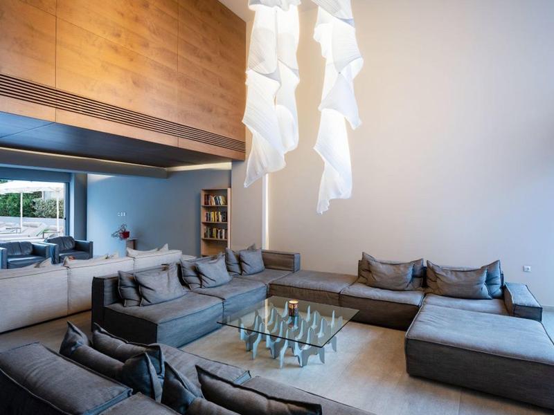 Modern living room with large gray sofas and glass coffee table under white hanging lamps.