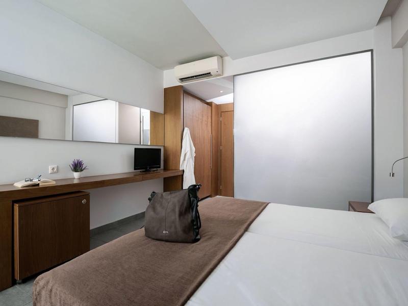 Modern hotel room with double bed, desk, mirrors, and simple decor.