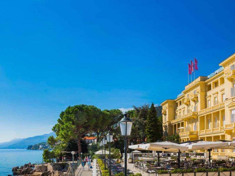 Jasny budynek hotelu z tarasem i drzewami pod czystym niebieskim niebem