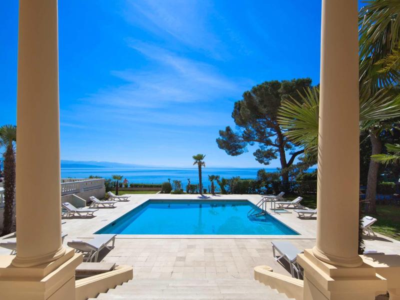 Widok na basen z morzem w tle, otoczony dwoma kolumnami przy czystym niebie.