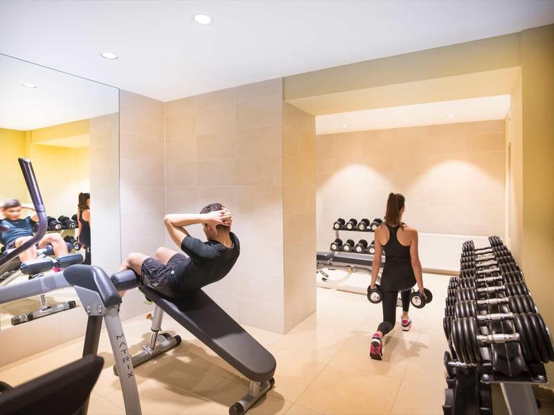 Nowoczesna siłownia z lustrami, ciężarami i sprzętem do ćwiczeń.