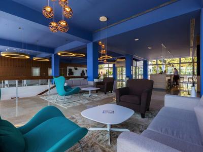 Nowoczesny hotelowy salon z wygodnymi fotelami, stolikami i stylowym oświetleniem.