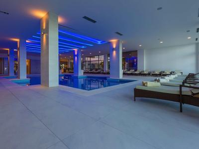 Nowoczesny kryty basen z niebieskim oświetleniem LED i leżakami w hotelu.