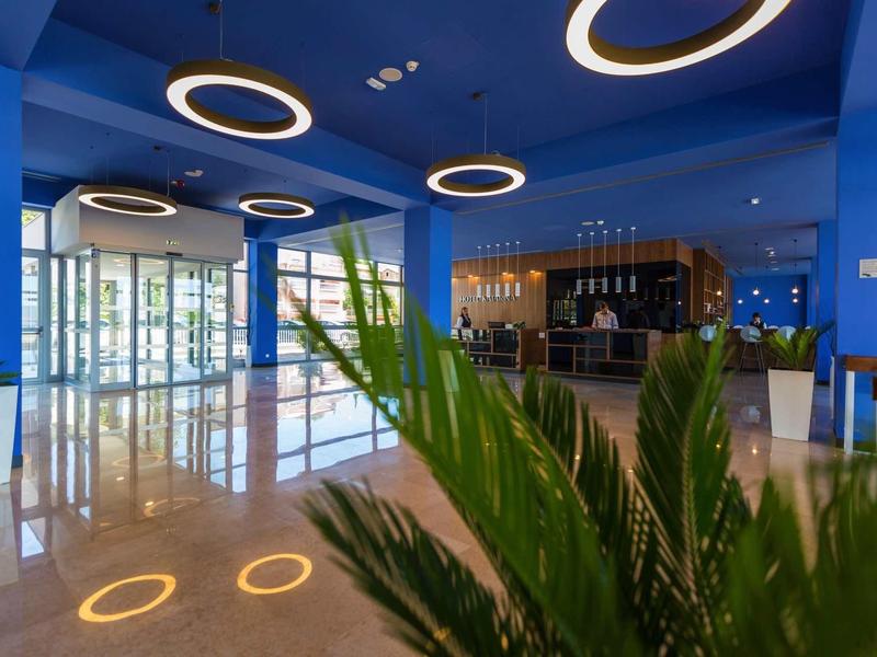 Nowoczesne lobby hotelowe z niebieskimi ścianami, okrągłymi lampami sufitowymi i roślinami.