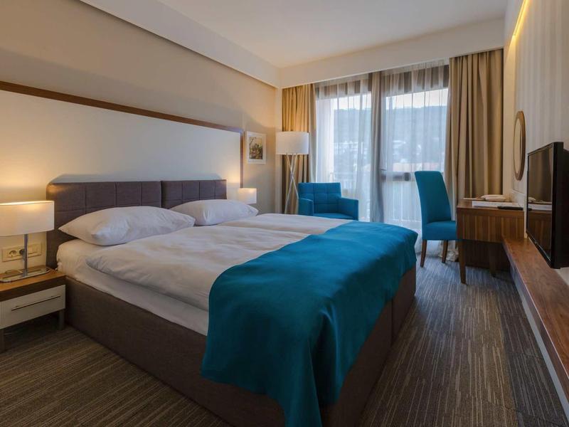 Nowoczesny pokój hotelowy z podwójnym łóżkiem, niebieskimi akcentami i balkonem z drzwiami szklanymi