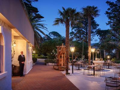 Terraza nocturna con sillas, mesas y palmeras junto a un edificio iluminado.
