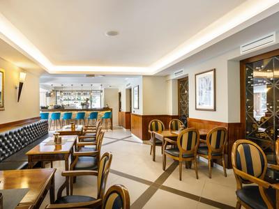 Elegante zona de bar de hotel con mesas de madera, sillas tapizadas y barra iluminada en la pared.