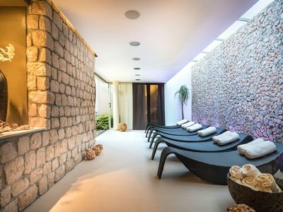 Sala de relajación con paredes de piedra y varias tumbonas negras con almohadas blancas.