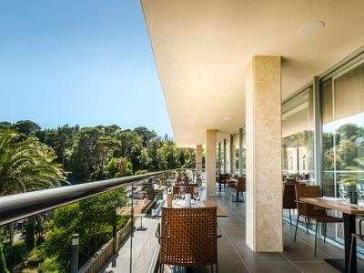 Balkon mit Sitzgelegenheiten und Blick auf Palmen und Natur unter blauem Himmel.