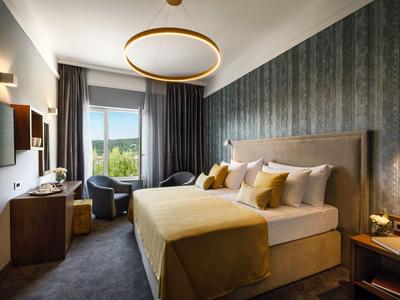 Modernes Hotelzimmer mit großem Bett, grünem Akzent, Sitzbereich und Fenster mit Blick ins Grüne.