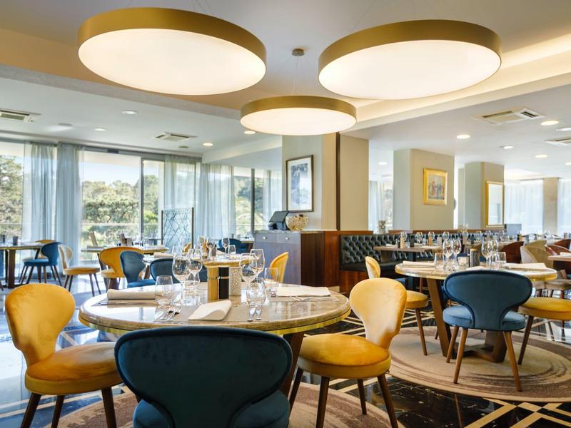 Restaurante moderno de hotel con mesas redondas, sillas variadas y grandes lámparas de techo circulares.