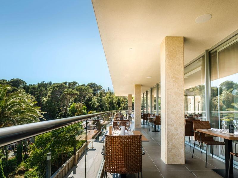 Balcón con sillas y mesas con vista a áreas verdes y cielo azul en un hotel.