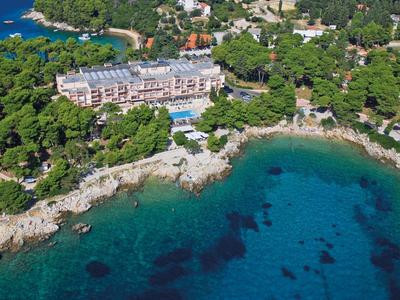 Letecký pohled na hotel s bazénem na skalnatém pobřeží s čistou modrou vodou a zelenými stromy.