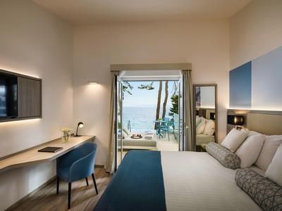 Moderní hotelový pokoj s výhledem na moře, manželskou postelí, pracovním stolem a terasou.