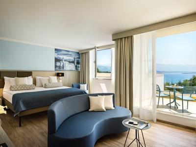 Moderne hotelkamer met tweepersoonsbed, bank en balkon met uitzicht op zee.