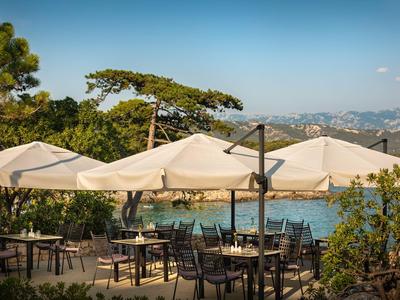 Buiten een hotel staan tafels met stoelen onder grote parasols, omringd door bomen en uitzicht op bergen.