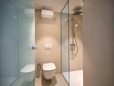 Moderní hotelová koupelna s bezbariérovým sprchovým koutem, toaletou a béžovými dlaždicemi.