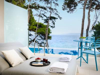 Terasa s posezením s výhledem na bazén a moře, obklopená stromy.